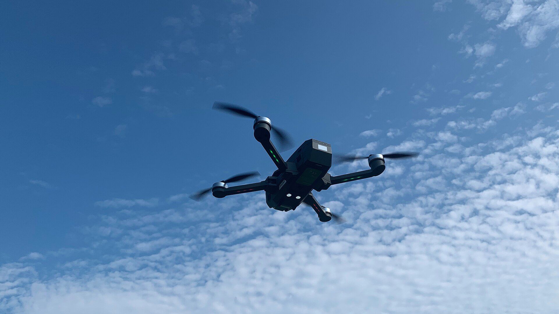Açık mavi gökyüzünde uçan dört pervaneli bir dron.