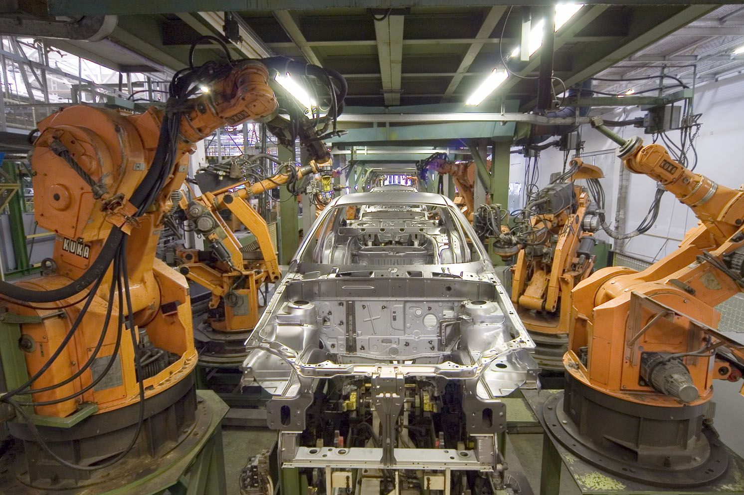 Bir otomobil üretim hattında çalışan turuncu endüstriyel robot kolları.